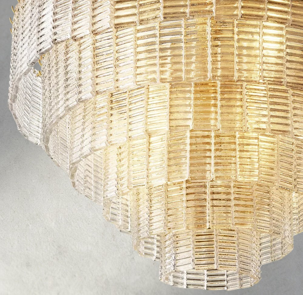 Lampthe Sirene clear glass round chandelier with textured glass cascading in concentric rings, refracting warm light.