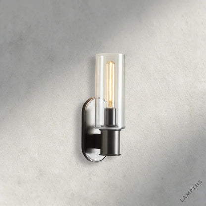 Lampthe Harlin Sconce in clear glass with a dark metal base and exposed Edison bulb, featuring modern sophistication.